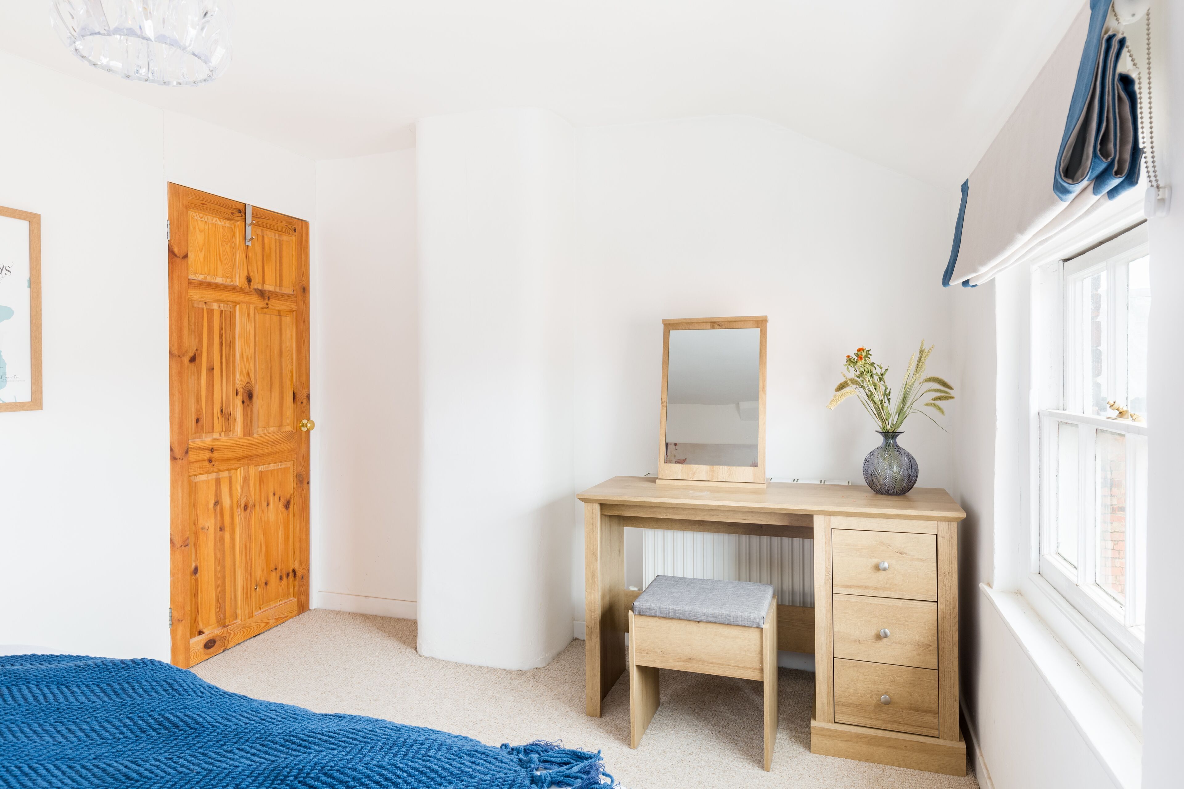 A bedroom with a wooden wardrobe, a wooden desk with a mirror, a small bench, and a window with curtains.