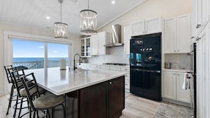 A modern kitchen with a large island, white cabinetry, stainless steel appliances, and a view to the ocean. - Beachfront 6BR, Two Decks, Pool Table + Game Room (Ponte Vedra Beach)