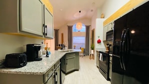 A modern kitchen with granite countertops, a black refrigerator, and a dining area in the background. - 4 Bedroom South Facing Pool Gem! (Haines)