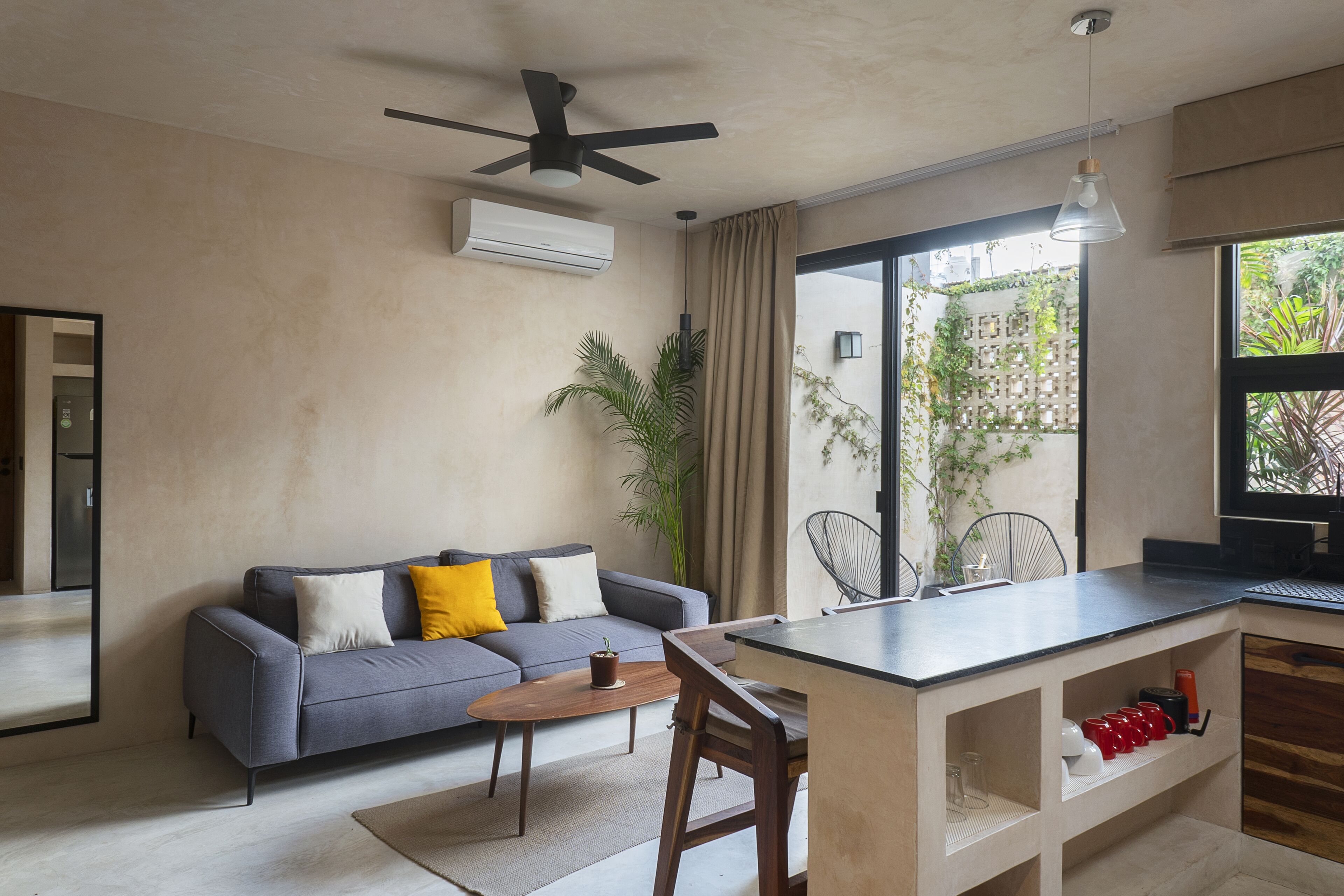 A modern living area with a grey sofa, wooden coffee table, and a small kitchen area with a bar counter.