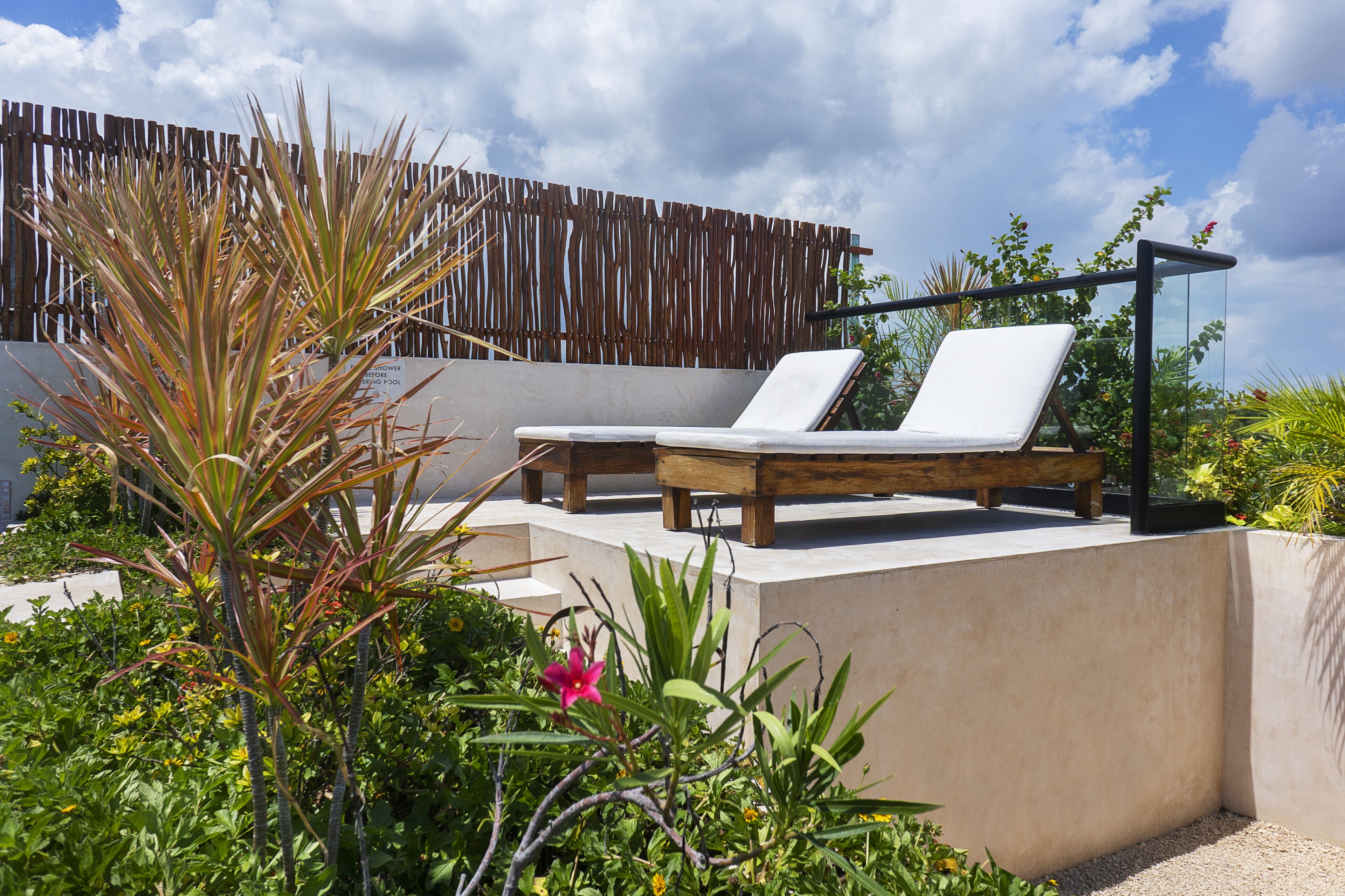 A rooftop lounge with two white lounge chairs, a wooden fence, and various plants.