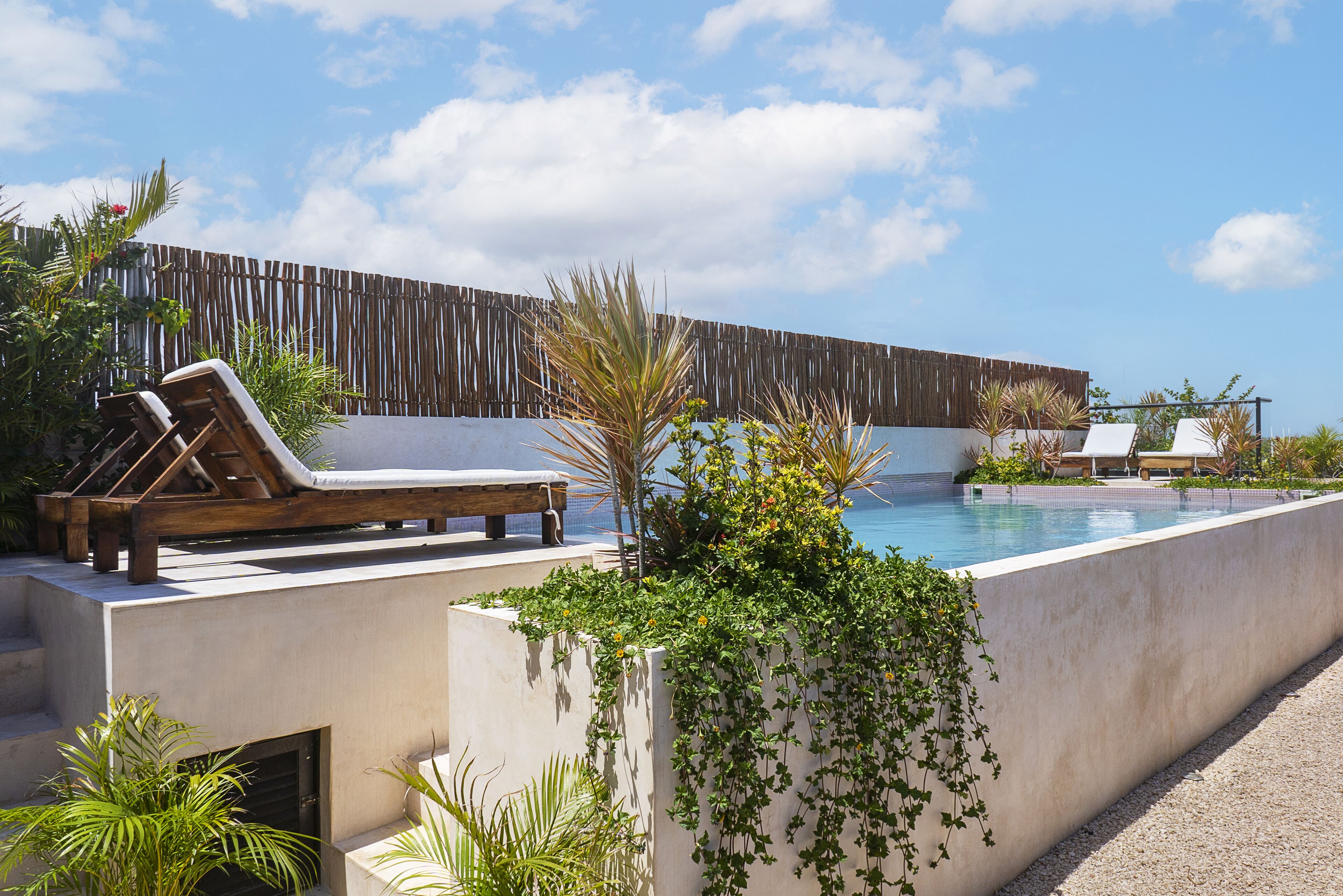 Zona junto a la piscina con sillones de descanso, valla de madera y vegetación.