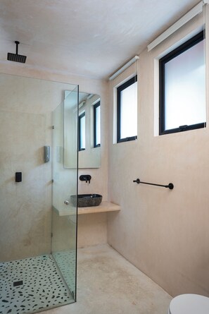 A modern bathroom with a glass shower enclosure, a sink with a black faucet, and a toilet. - UJO Tulum (Tulum)