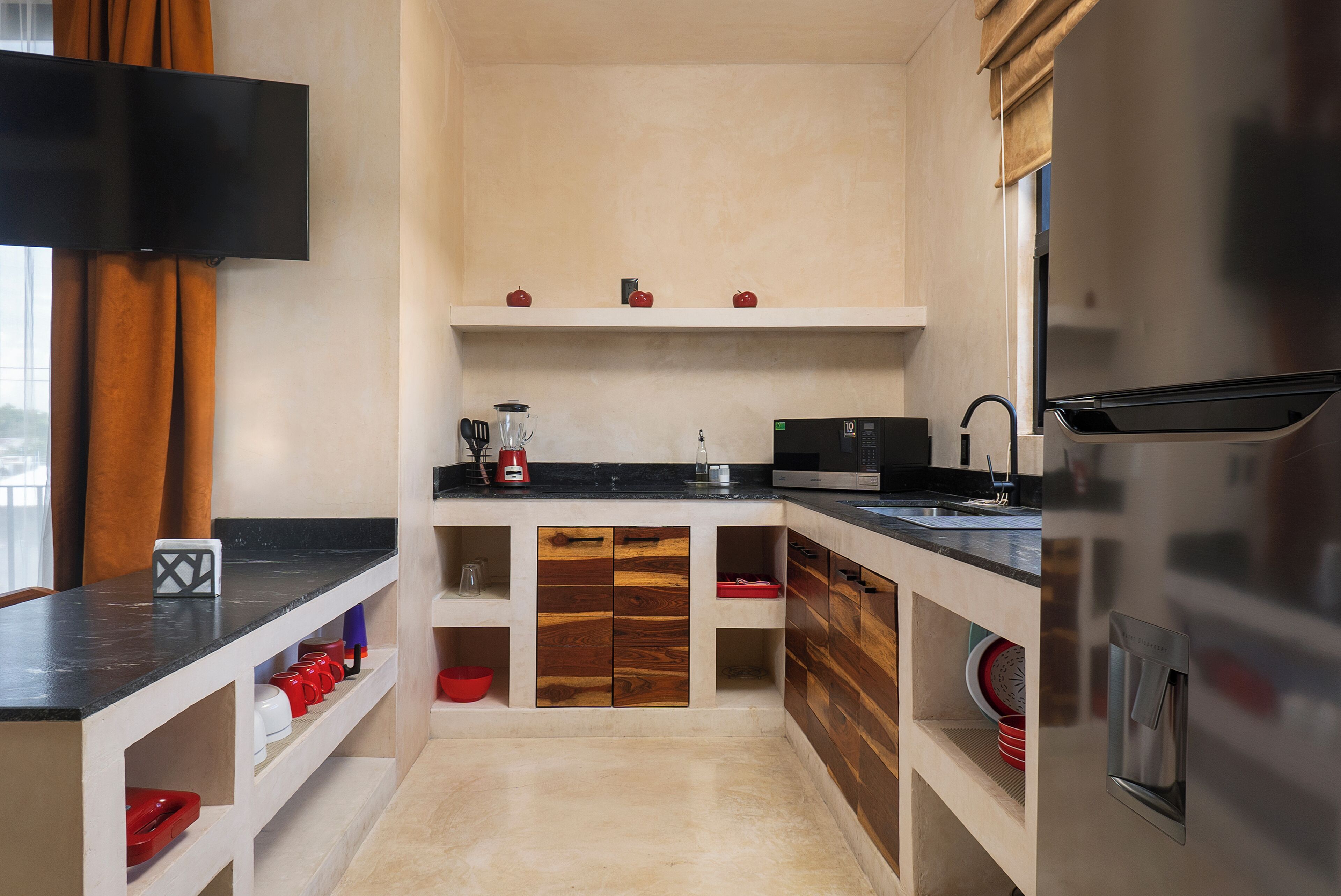 A compact kitchen with a flat-screen TV, wooden cabinets, a microwave, and a stainless steel refrigerator.