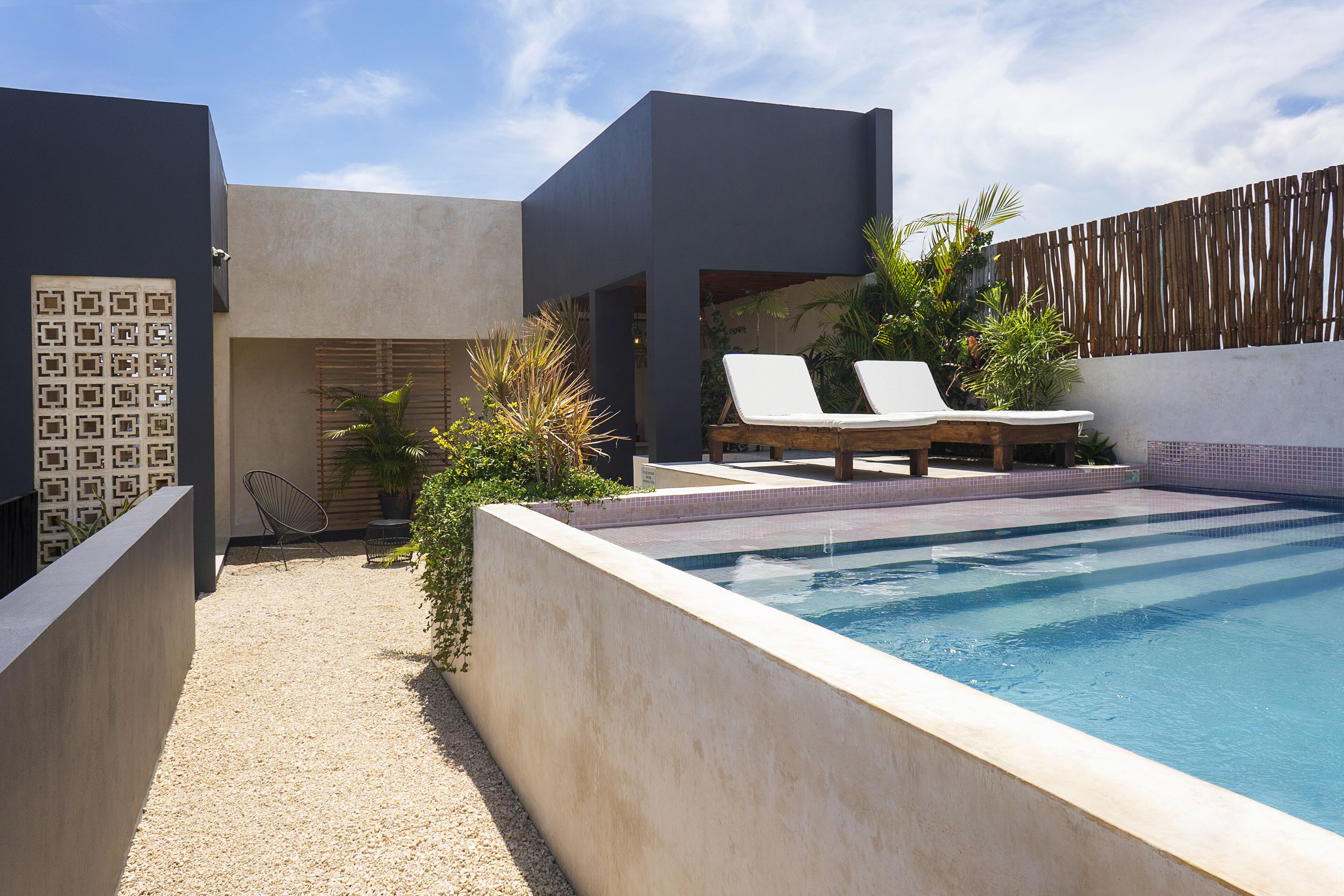 A modern outdoor pool area with two lounge chairs, a small garden, and a tiled deck.