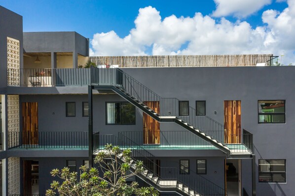 Un immeuble à plusieurs étages, doté d’un escalier reliant les différents niveaux, de grandes fenêtres et d’un balcon avec une balustrade.