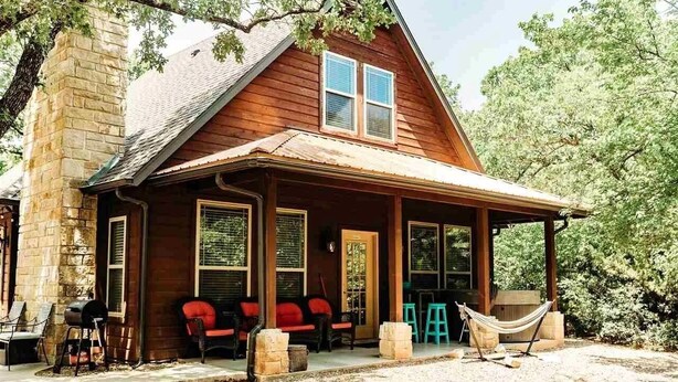 Una casa de madera con porche, chimenea de piedra y mobiliario exterior.