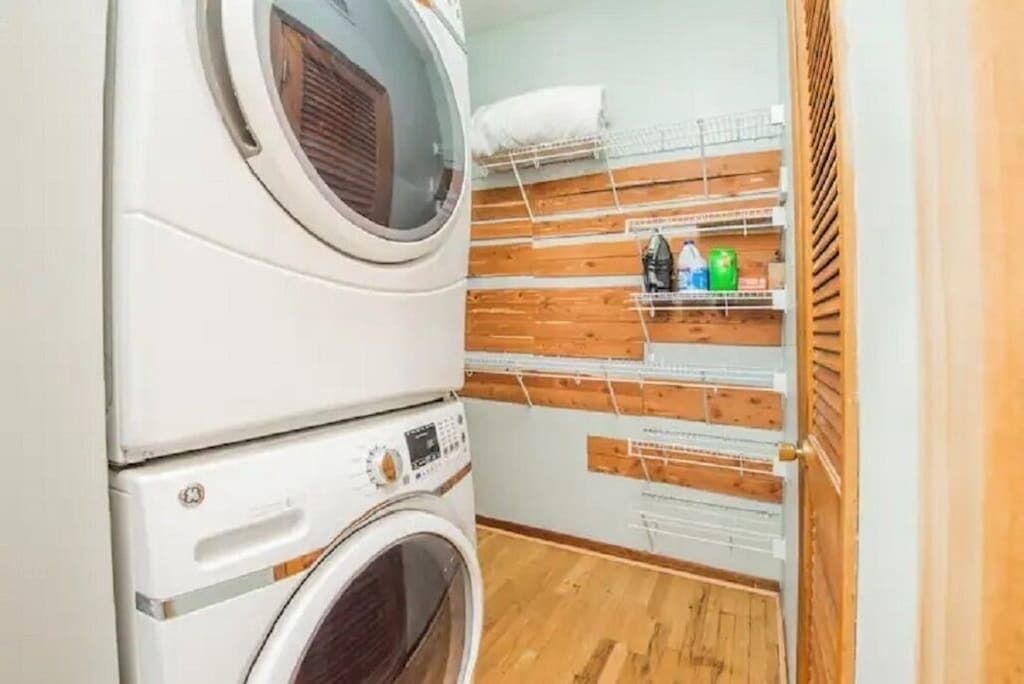 Un área de lavandería con lavadoras apiladas y un estante con productos de limpieza.