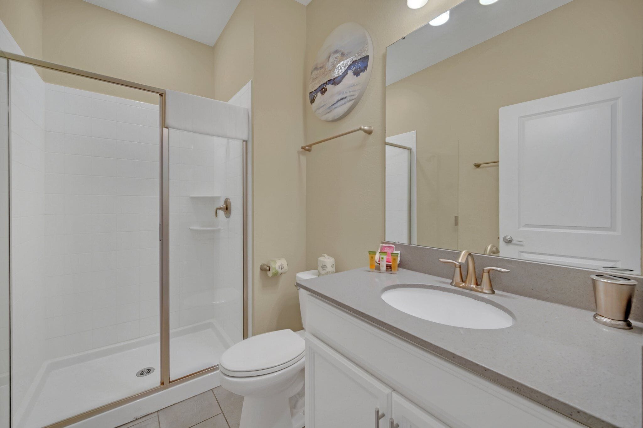 A modern bathroom with a glass-enclosed shower, a white toilet, and a vanity with a sink and mirror.