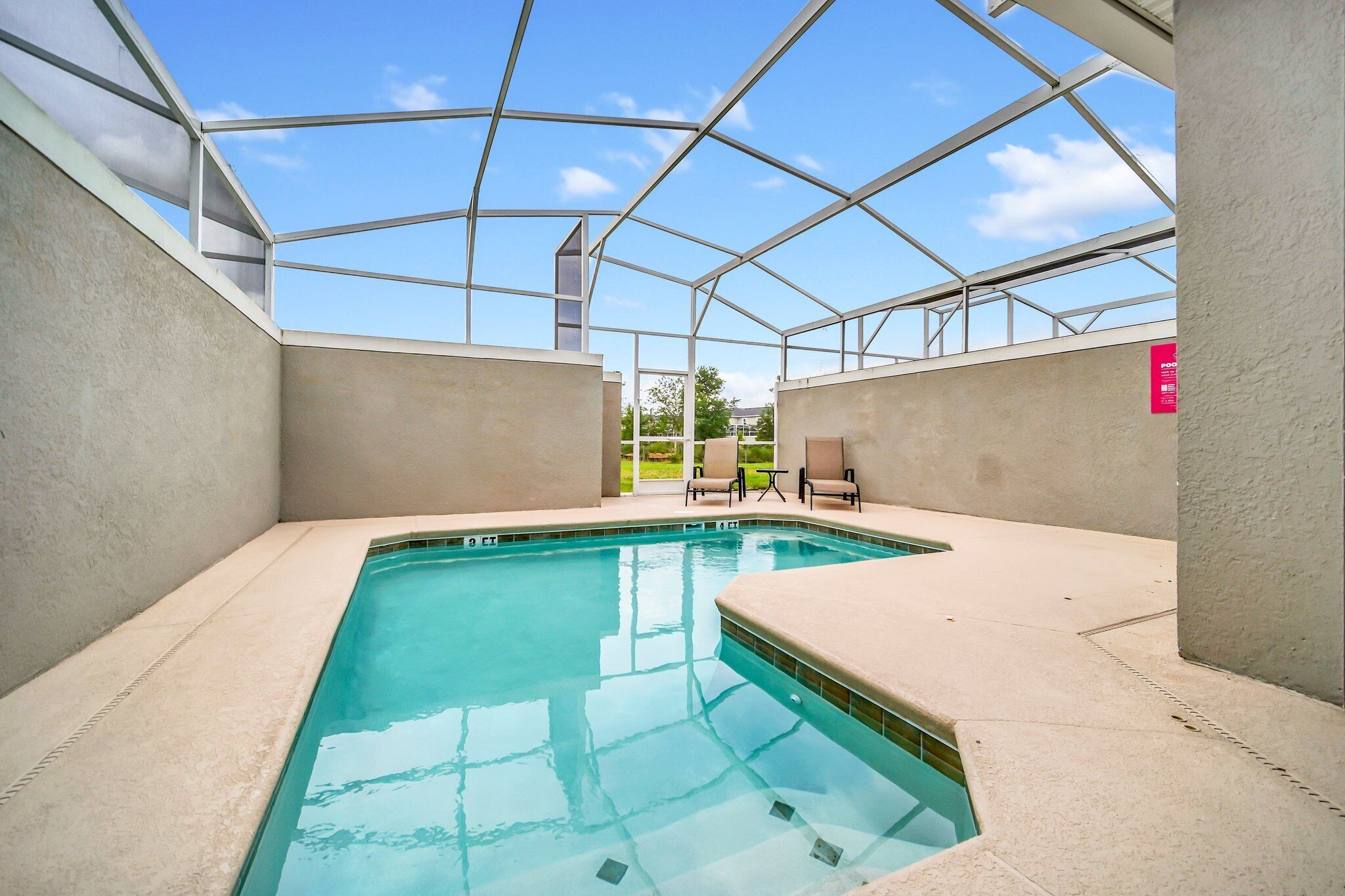 An indoor swimming pool with a clear glass ceiling, beige walls, and a few chairs.