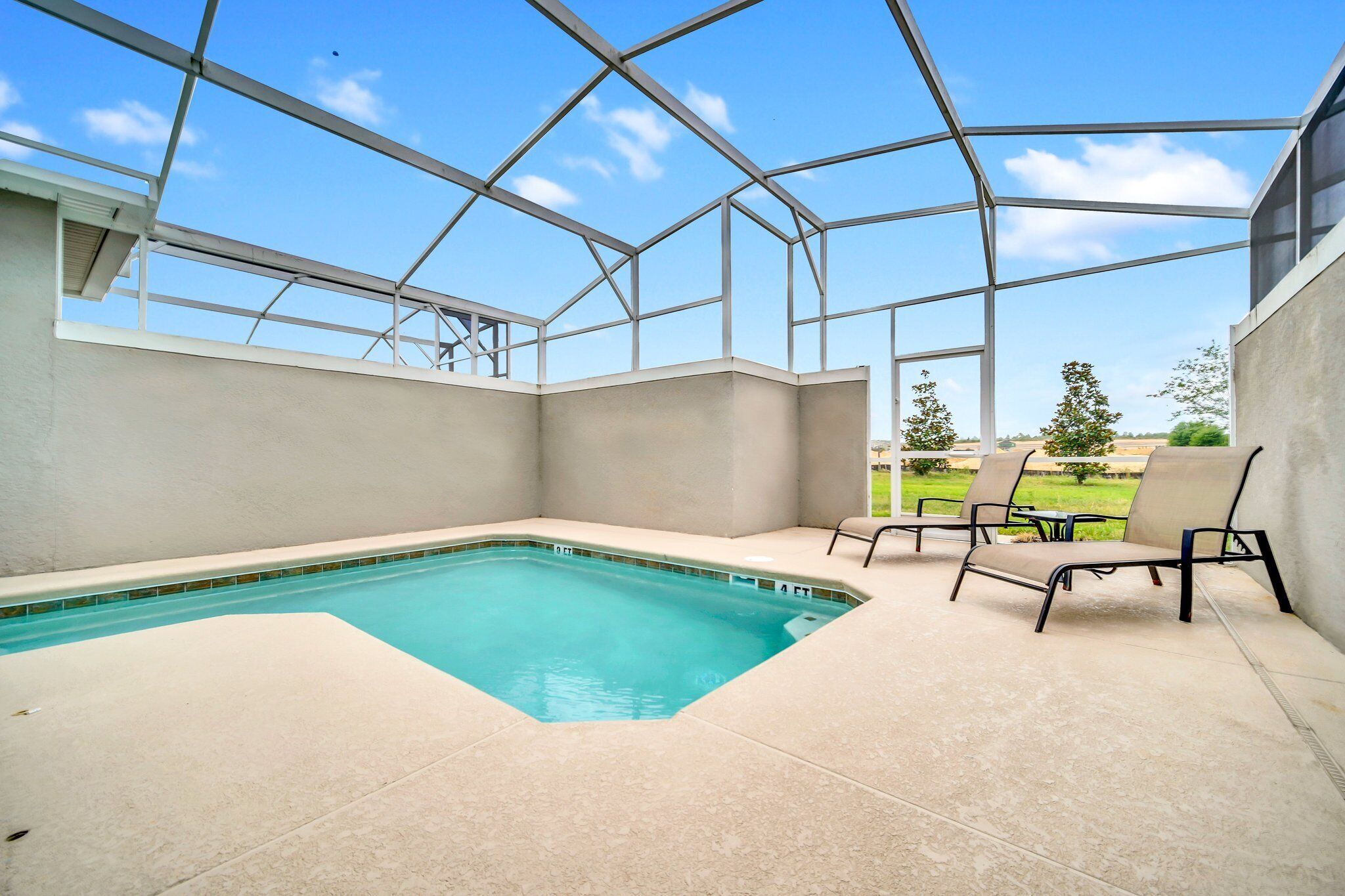 A covered outdoor swimming pool with a clear view of the sky and a grassy area in the background.