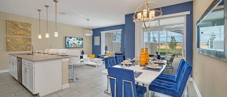 Een moderne keuken met een centraal eiland, een zithoek met blauwe gestoffeerde stoelen, en een groot raam met uitzicht op de omgeving.