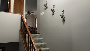 Una escalera con barandillas de madera que lleva a un comedor con un ventilador de techo y una lámpara de pared.