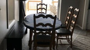 Un comedor con una mesa redonda y cuatro sillas, una ventana con cortinas y un letrero colgado en la pared.