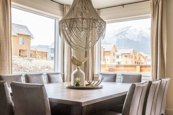 A dining area with a large table, six chairs, a decorative vase, and a unique hanging light fixture.