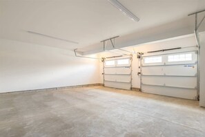 Eine saubere, leere Garage mit zwei großen Garagentoren, einem Betonboden und Deckenleuchten.