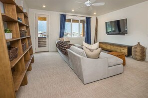 Ein modernes Wohnzimmer mit einer Couch, einem Fernseher, einem Bücherregal und einem Fenster mit Vorhängen.