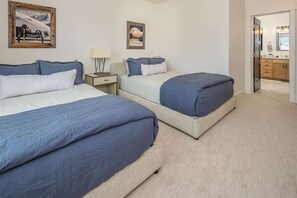 Ein Hotelzimmer mit zwei Betten, einem Nachttisch, einer Lampe sowie einer Tür zu einem Badezimmer und einer Küche.