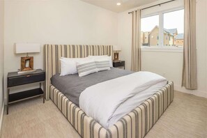 Hotellihuone, jossa on sänky, kaksi yöpöytää, ikkuna verhoilla ja näkymä ulkona oleviin rakennuksiin.