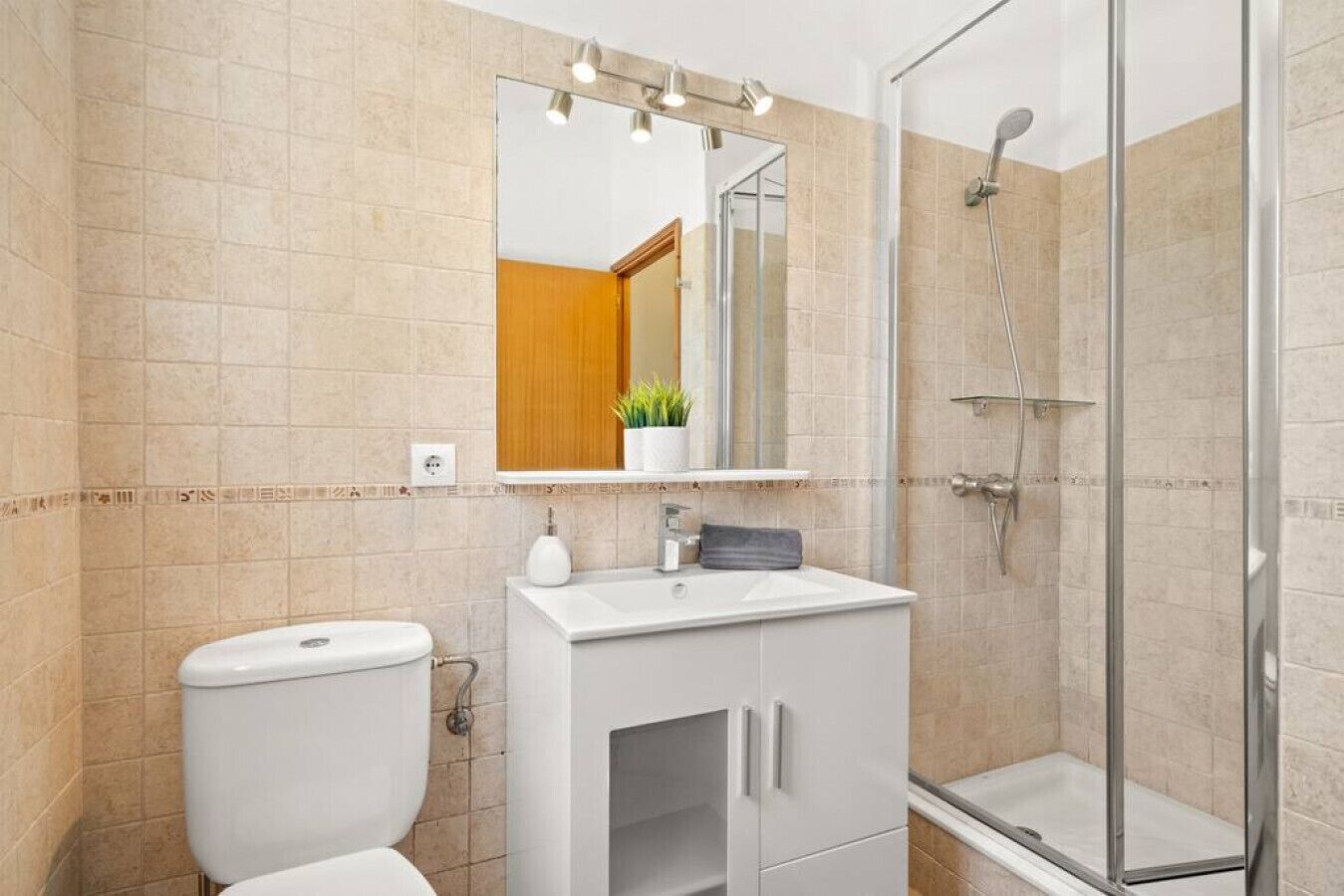 Ein Badezimmer mit Toilette, Waschbecken, Spiegel, Dusche und gefliesten Wänden.
