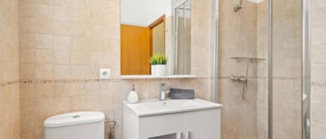 Ein Badezimmer mit Toilette, Waschbecken, Spiegel, Dusche und gefliesten Wänden.