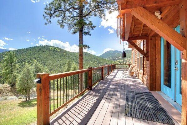 A wooden deck with a metal railing, a blue door, and a view of a forested mountain range.