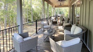 A covered outdoor deck with wicker furniture, ceiling fans, and a view of the surrounding forest. - Lakefront-Lakeview-Steps to the Water-Tim's Ford Lake LUXURY Home & DOCK (Winchester)