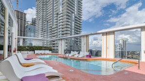 Un área de piscina en la azotea con sillones y vistas a edificios altos.