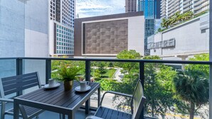 Un balcón con una mesa y sillas, una planta en maceta y vistas de un paisaje urbano con edificios altos.
