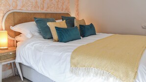 A neatly made bed with white linens and multiple pillows in various colors, a bedside table with a lamp, and a patterned wall in the background. - 1 bedroom accommodation in Dronfield (Dronfield)