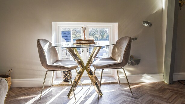 A dining area with a glass table and two chairs, a window with a view, and a herringbone wood floor. - 1 bedroom accommodation in Dronfield (Dronfield)