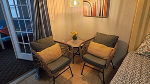 Una habitación con dos sillones de mimbre, una mesita con un florero y un cuadro en la pared, y una cama con ropa de cama estampada.
