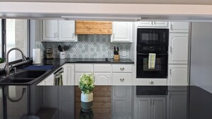 Una cocina moderna con armarios blancos, encimera negra, protector contra salpicaduras de madera y horno negro.