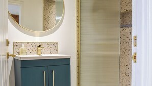 A bathroom with a round mirror, a sink with a gold faucet, and a spa bottle.