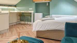 A compact room with a bed, a small kitchenette, and two bar stools.
