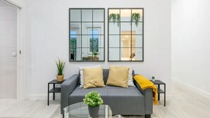 A modern living room with a grey sofa, two cushions, a glass coffee table with a plant, and two black side tables with small plants. - Your home in the center of Madrid (Madrid)