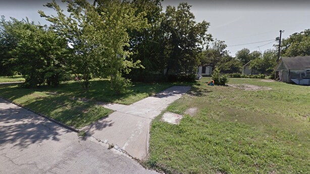 A residential area with a paved driveway leading to a house, surrounded by trees and a grassy lawn.
