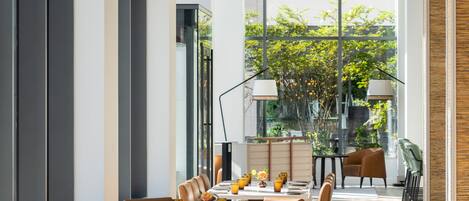 A modern restaurant with a long dining area, multiple tables, and hanging pendant lights.