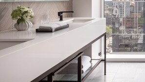 Un baño moderno con un espejo grande, un lavamanos blanco y vistas a la ciudad a través de amplias ventanas.