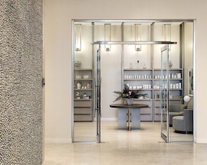 A modern interior with a glass partition, a central round table with a plant, and shelves with various items.