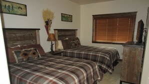 A bedroom with two beds, wooden headboards, a dresser, and a window with blinds. - Dual Queens Townhomes On the Green (Afton)