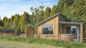 A wooden cabin with large windows, a balcony, and a view of a forested area.
