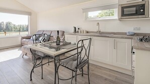 A modern kitchen with white cabinetry, a dining table with chairs, a microwave, and a view of the outdoors through a large window.