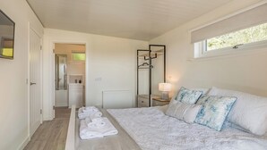 A bedroom with a bed, a bedside table with a lamp, a mirror, and a window.