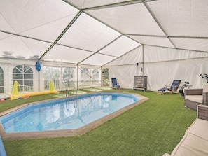 A covered swimming pool with artificial grass, lounge chairs, and a ceiling fan.