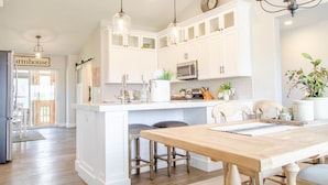 Una cocina con armarios blancos, una isla de madera con taburetes e iluminación colgante.