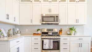 Una cocina con armarios blancos, horno de acero inoxidable, microondas y hervidor.