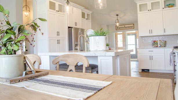 Una cocina con armarios blancos, una mesa de comedor de madera y lámparas colgantes.