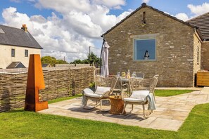 A stone building with a large window, outdoor seating with wicker chairs and a table, and a grassy patio area. - Luxurious Complex: 2 barns together edge of Frome (Frome)