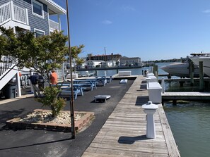 A waterfront dock with picnic tables, a small tree, and a building with a balcony.